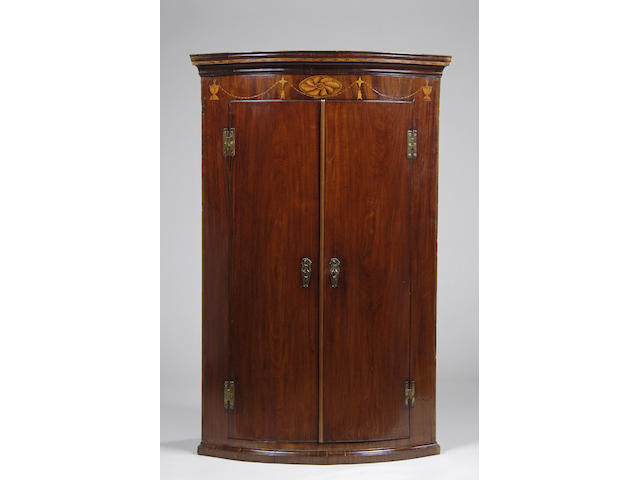 A George III mahogany bowfront inlaid hanging corner cupboard