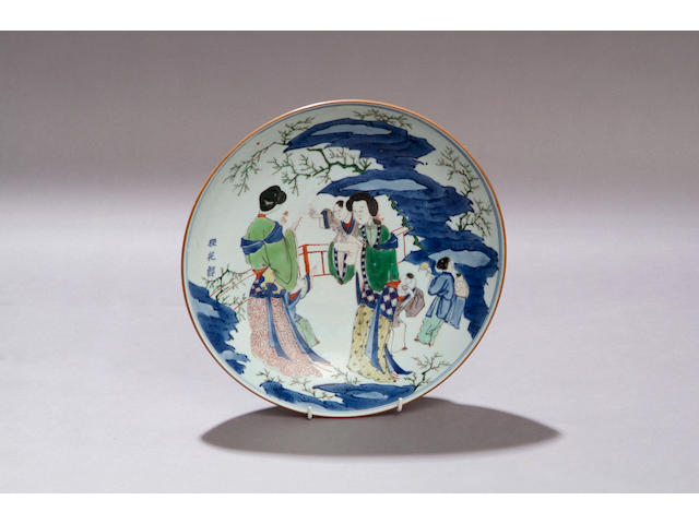 A Transitional saucer dish Decorated with court ladies and attendants in a garden in yellow, green, iron red and underglaze blue and incorporating three character inscription, 30cm diameter.