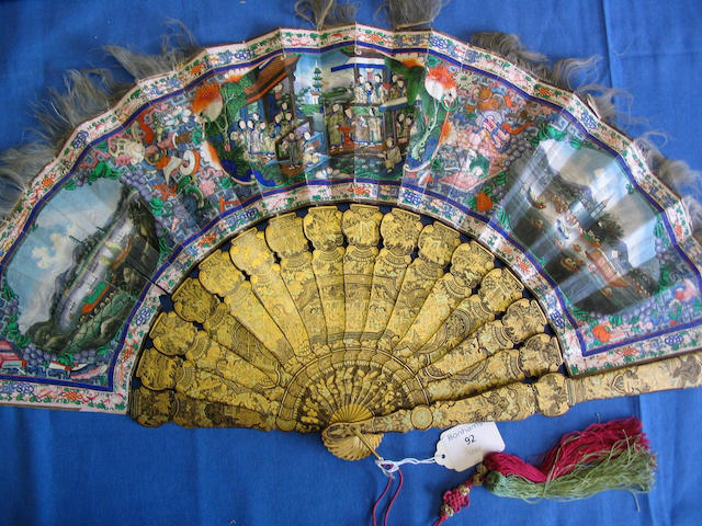 A good early 19th Century Chinese export fan The bright gold and black lacquer guards and sticks well-decorated with figures on terraces amid panels of birds, figures and objects, the leaf decorated to one side with ivory faced courtiers flanked by oval painted panels, one of a river scene, the other a trade port, all amid objects and animals within a formal border edged with feathers, the reverse with numerous ivory faced figures arranged on terraces, balconies and other defined areas within a conforming border, very minor damage, 32cm.