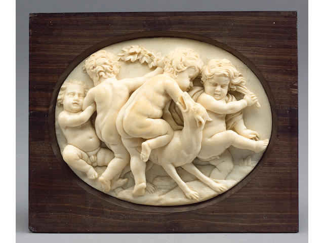 A late 18th / early 19th century South German carved ivory oval relief of four playful putti with a hound