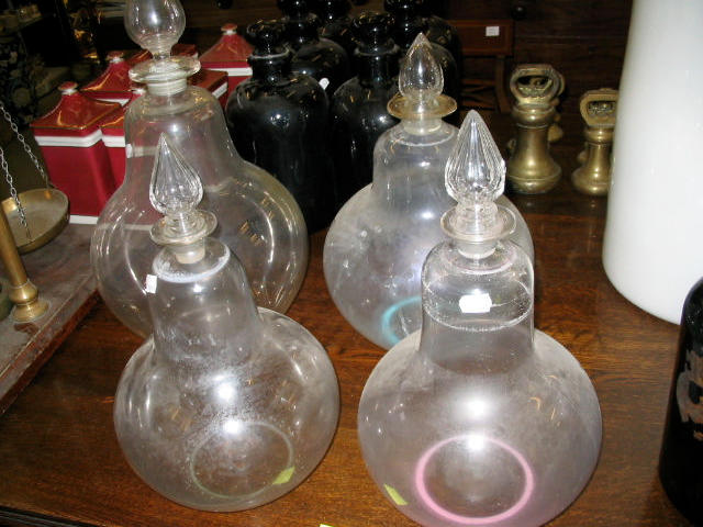 A set of three glass carboys and stoppers, and another larger.