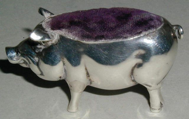 A silver pincushion in the form of a standing pig,