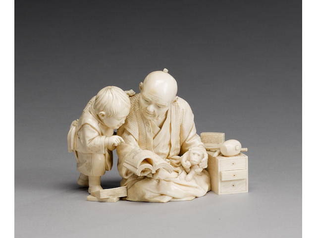 An ivory okimono carved as a boy and his father looking at an ehon;