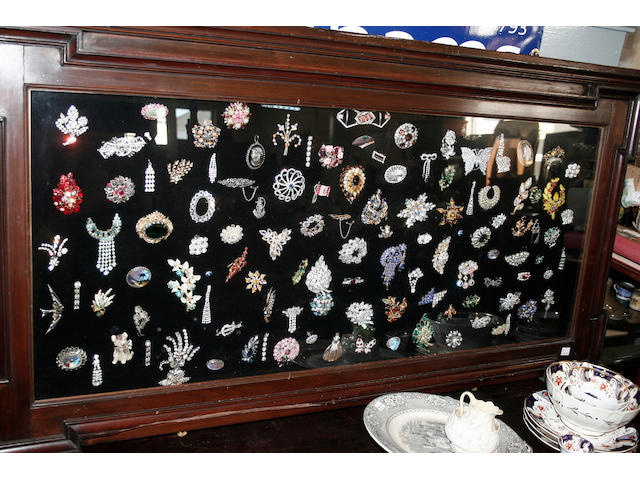 A framed and glazed display of approximately one hundred costume jewellery brooches,