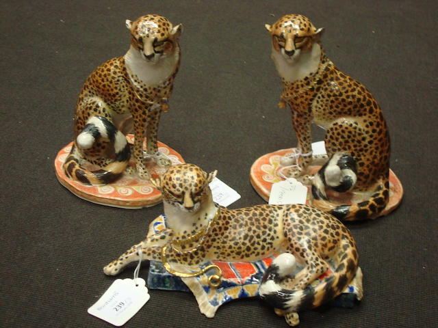 A pair of modern porcelain models of seated cheetahs and another similar model of a recumbent cheetah, all modelled by Anne Gordon