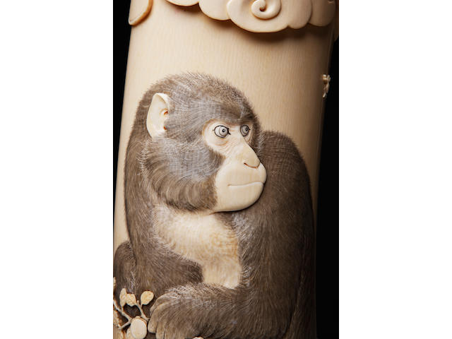 A large ivory tusk tusk carved with a monkey, on wood stand