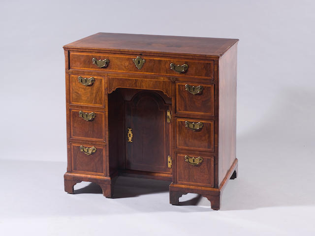 An early 18th century walnut kneehole deskFitted on an array of feather banded drawers, around a recessed cupboard, on bracket feet, 78cm wide.