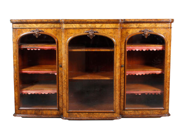 A Victorian figured walnut dwarf breakfront bookcase, fitted with adjustable shelves enclosed by three arched glazed doors, with carved leaf scroll ornament, on a moulded plinth base, 176cm.