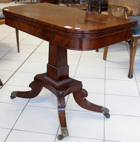 A late Regency mahogany card table, the hinged 'D' shape fold over top on a square tapering pillar with gadrooned collar, the concave sided platform on palmette headed reeded downswept quadripartite base, brass claw caps and castors.