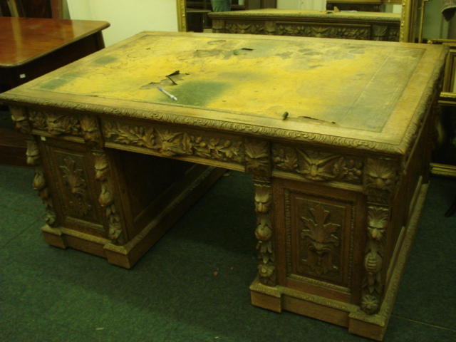 A partner's Victorian oak desk, of panelled construction, heavily carved with masks, oak leaves, acorns, flowers and fruits, the inset rectangular top above three frieze drawers and six pedestal drawers enclosed by a pair of doors, opposed by three frieze drawers and a pair of cupboards fitted with sliding trays, on inverted breakfront plinth bases, 153 x 100cm.