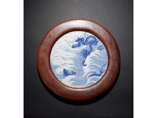 A blue and white plaque of circular form decorated with a Dragon beside two Carp, leaping above waves Kangxi six-character mark and of the period