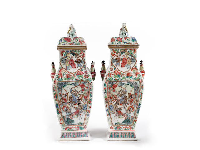 A large pair of Canton famille rose vases and cover, 19th Century, each of baluster form, enamelled on each of the main sides with a rectangular panel enclosing figures engaged in combat or within a court setting, all with similar shaped cartouches to the necks, all amidst birds and butterflies, amidst melon and peach sprigs each blossoming peony and leaves, inset to each side with moulded handles in the form of ladies seated on lotus, the covers surmounted by finials in the form of seated ladies, 55.5cm high. (4)