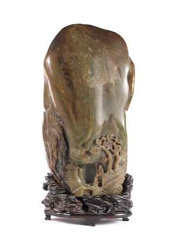 A large green jade mountain group, late 19th/early 20th Century, carved with shouloo and an attendant within a landscape, together with a wood stand, 29cm high. ((2)).