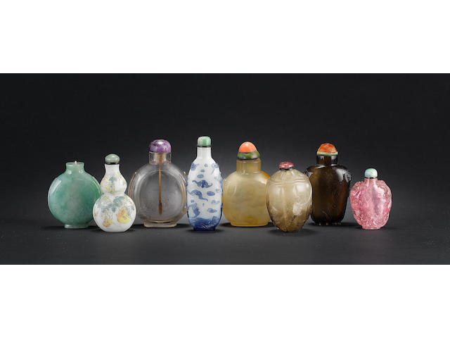 A mixed group of 8 snuff bottles, comprising: 3 crystal, 1 chalcedony, 1 jadeite, 1 blue overlay with bats, 1 rose quartz and 1 enamelled glass bottle of double gourd form (one missing stopper)