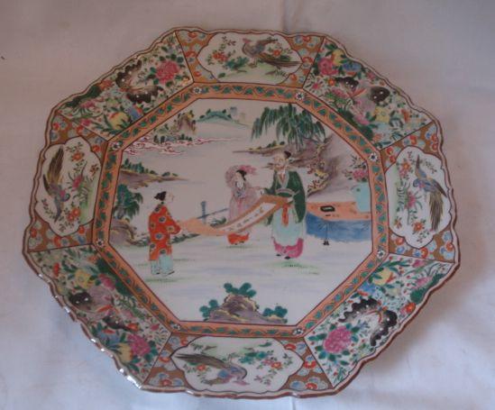 A large late 19th Century Chinese famille decorated charger, octagonal wavy edge form with central panels of figures lookinat a scroll with flower an bird panel borders, 43cm.