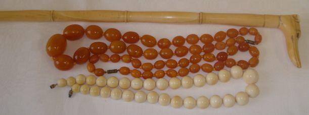 An early 20th Century sectional carved ivory walking cane,the handle carved as a hounds hand, 90cm, a string of graduated ivory beads, circa 1920, 50cm, and two strings of butterscotch amber the oval beads graduated from 10mm to 32mm.
