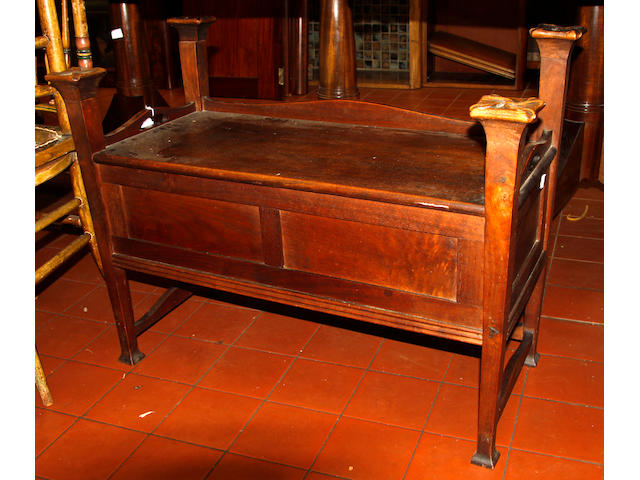 An Art Nouveau mahogany organ stool, in the manner of C A Voysey, the rectangular seat with an undulating gallery, with cut-out carrying handles, music compartment below enclosed by a hinged fall front with spot hammered mounts, on tapering square section legs with spreading bases and carved capitals united by undulating stretchers, 81cm.