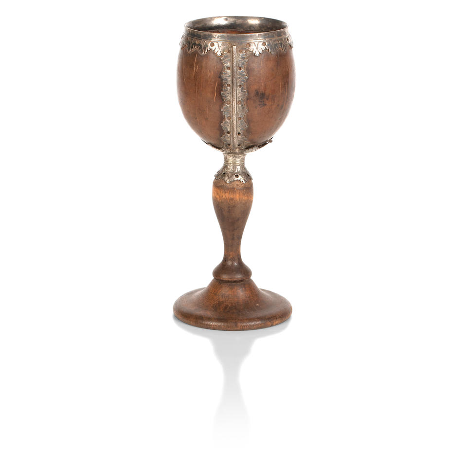 A George III white-metal mounted coconut cup with a later turned wood base, together with four more coconut cups and a carved coconut drinking vessel 18th and 19th century  (6)